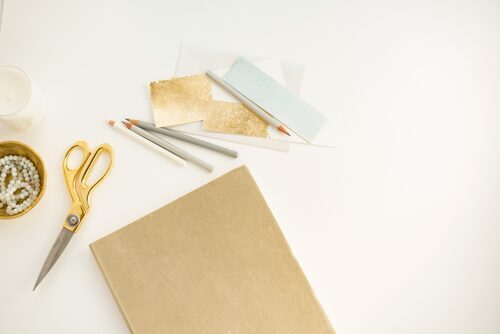 Goldene Schere, Papier und Stifte auf hellem Hintergrund 